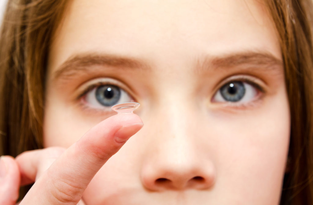 Girl with hazel eyes holding contact lens with finger while looking at camera