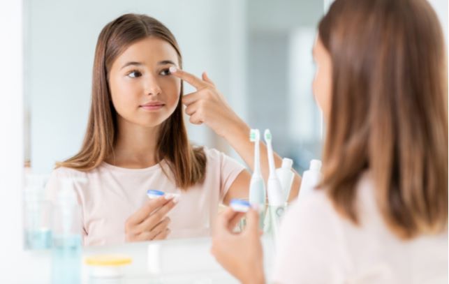 Girl putting on ortho-k lenses while looking at self in mirror