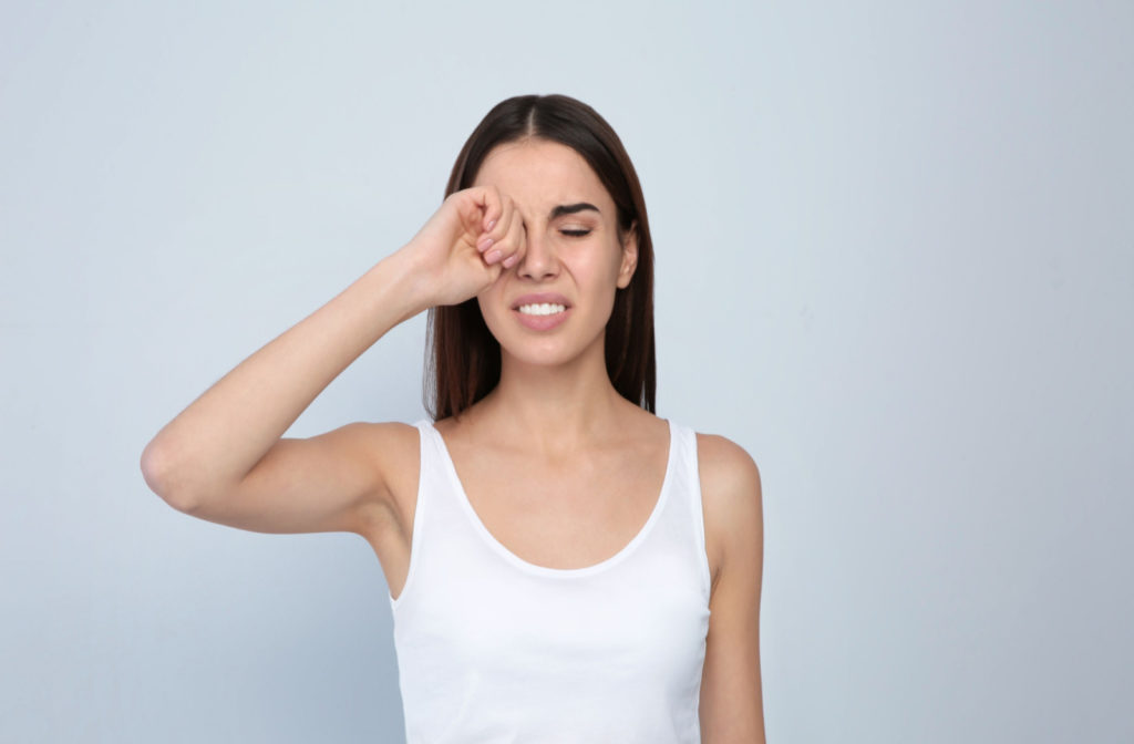 a woman rubs her eye in pain due to blepharitis
