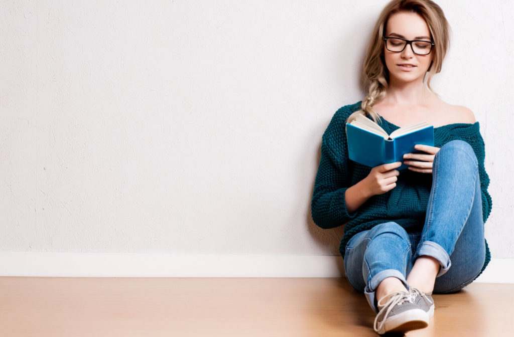 A young woman is reading a book at ease with her Miyosmart lens eyeglasses on while sitting on the floor.