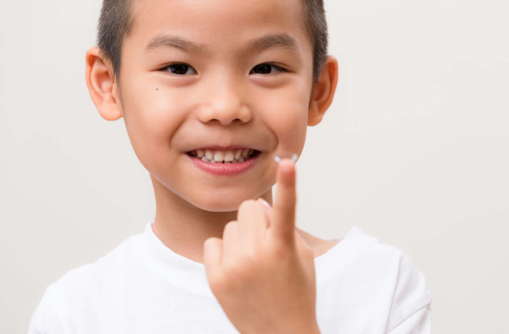 A young boy holding a single ortho-k contact lens on his finger.