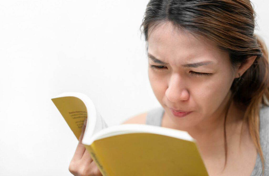 Close-up of a young woman holding a yellow book and squinting to read it