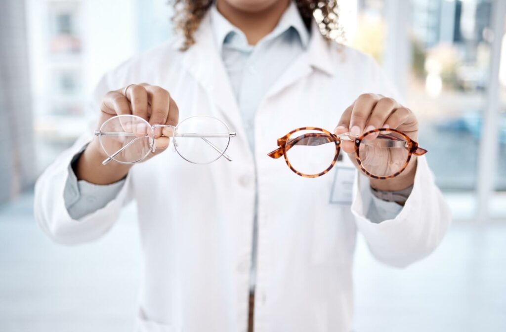 An eye doctor holds up two pairs of glasses, one with clear frames and the other with tortoiseshell frames.