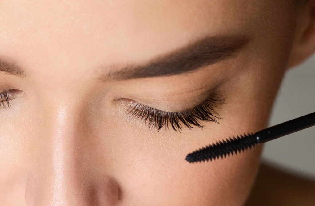 A close-up of a person's upper face as they apply mascara.