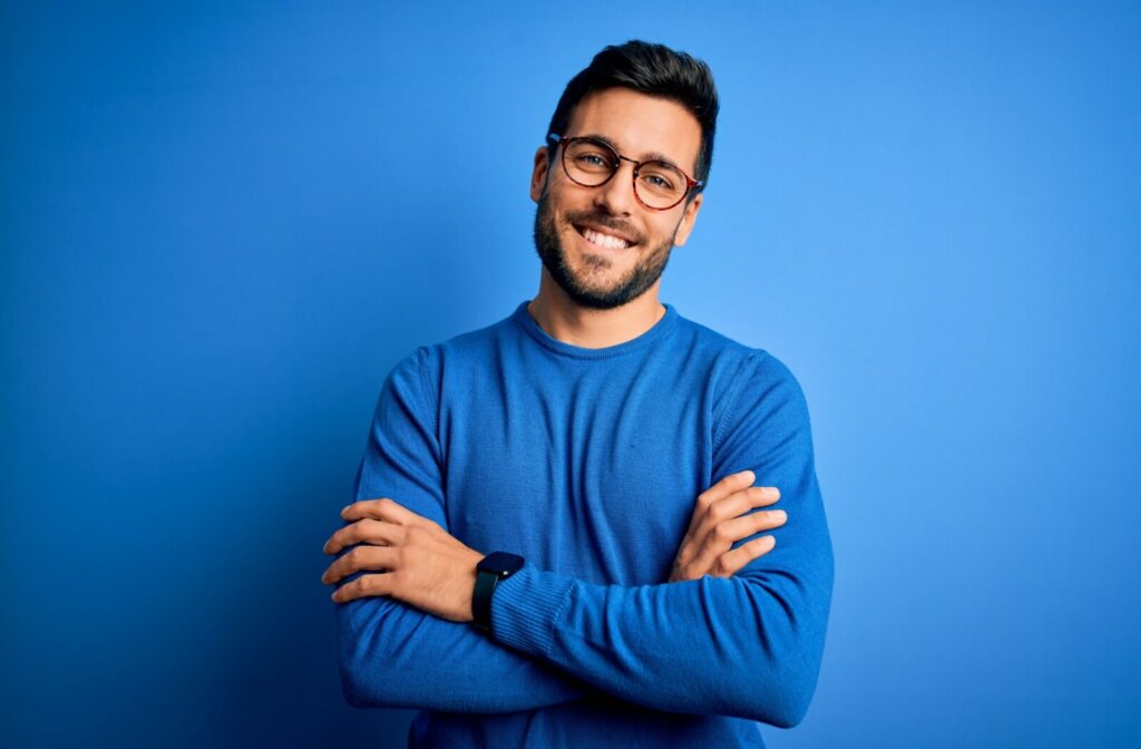 Smiling man with glasses standing with arms crossed against a solid blue background.