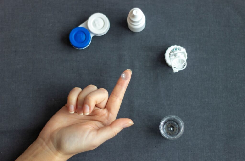 An ortho-k lens resting on a fingertip, surrounded by contact lens cases.