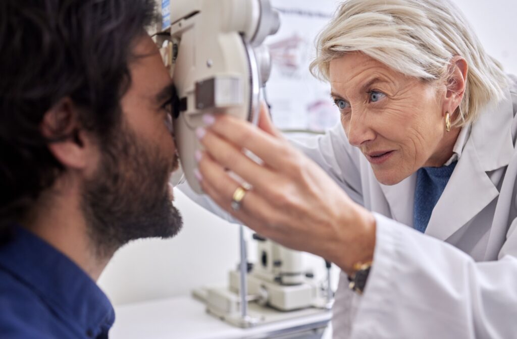 Eye doctor in a white lab coat holds instrument to paitents eyes, concentrating on the exam. Patient sits comfortably and smiles.