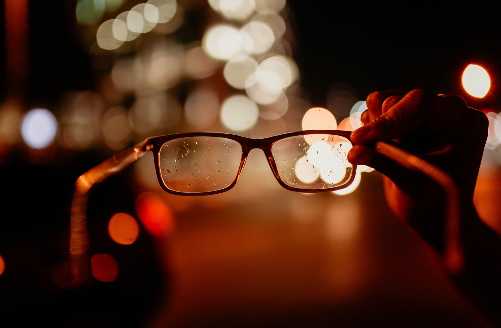 Close up of person holding glasses, with a bokeh background; Astigmatic blur.