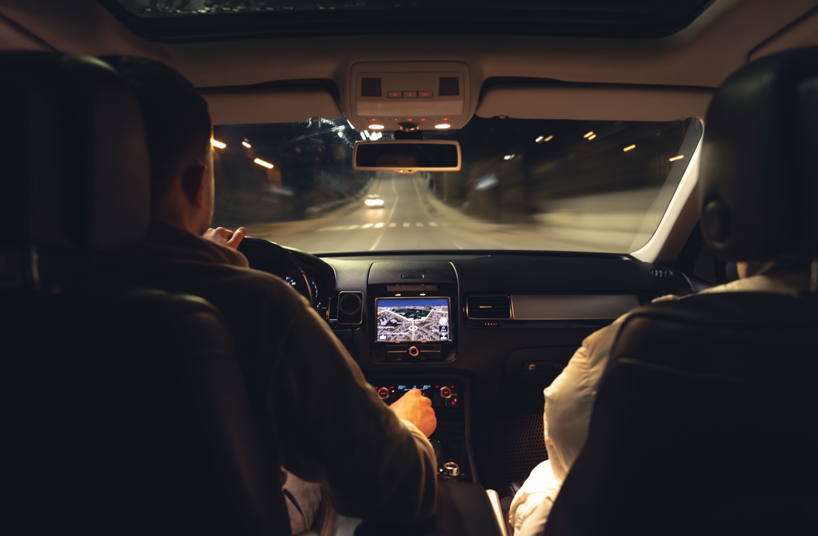 View from behind of a couple driving together down a nighttime road.