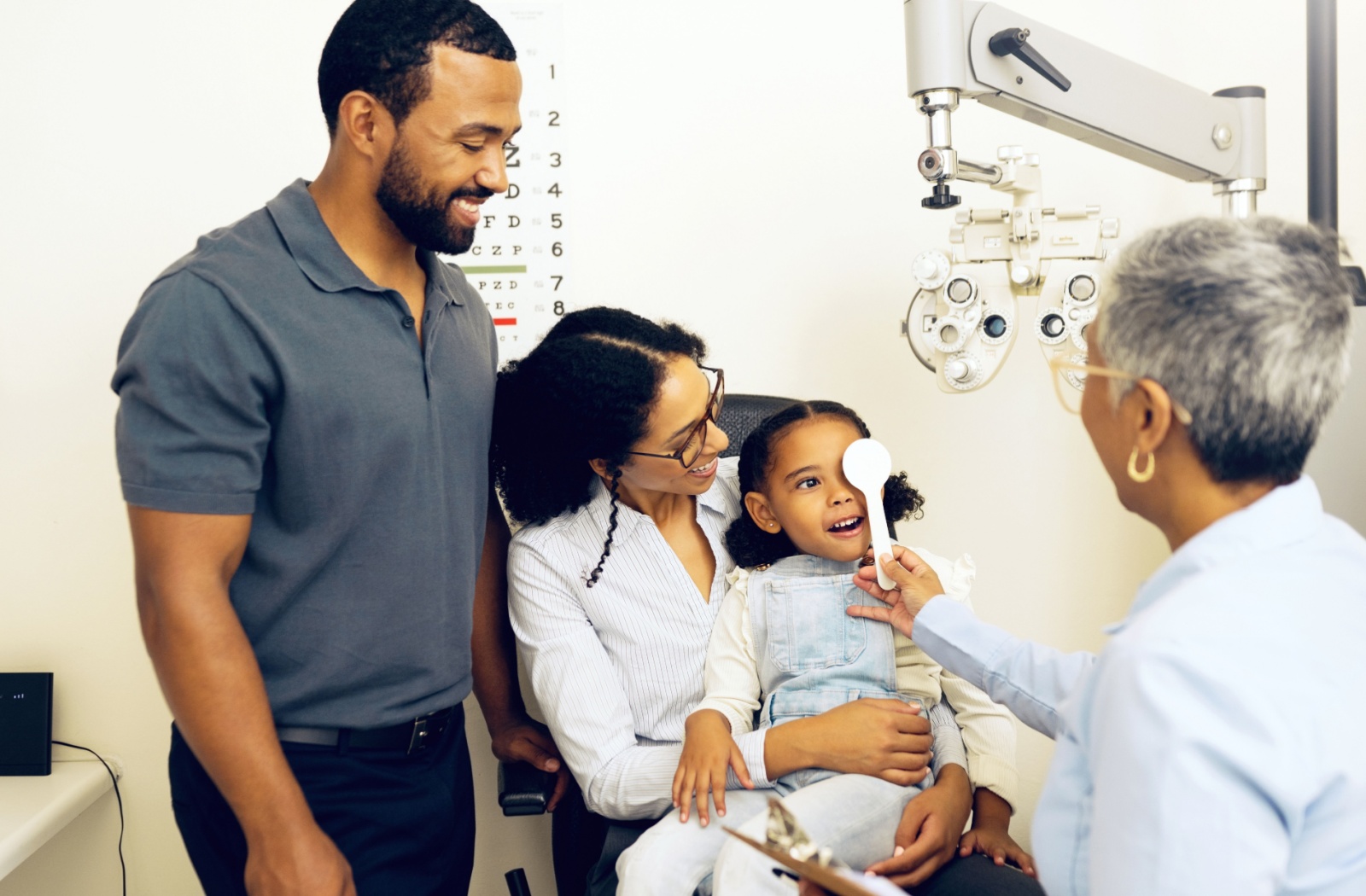 An optometrist tests a child's vision while her parents look on cheerfully.