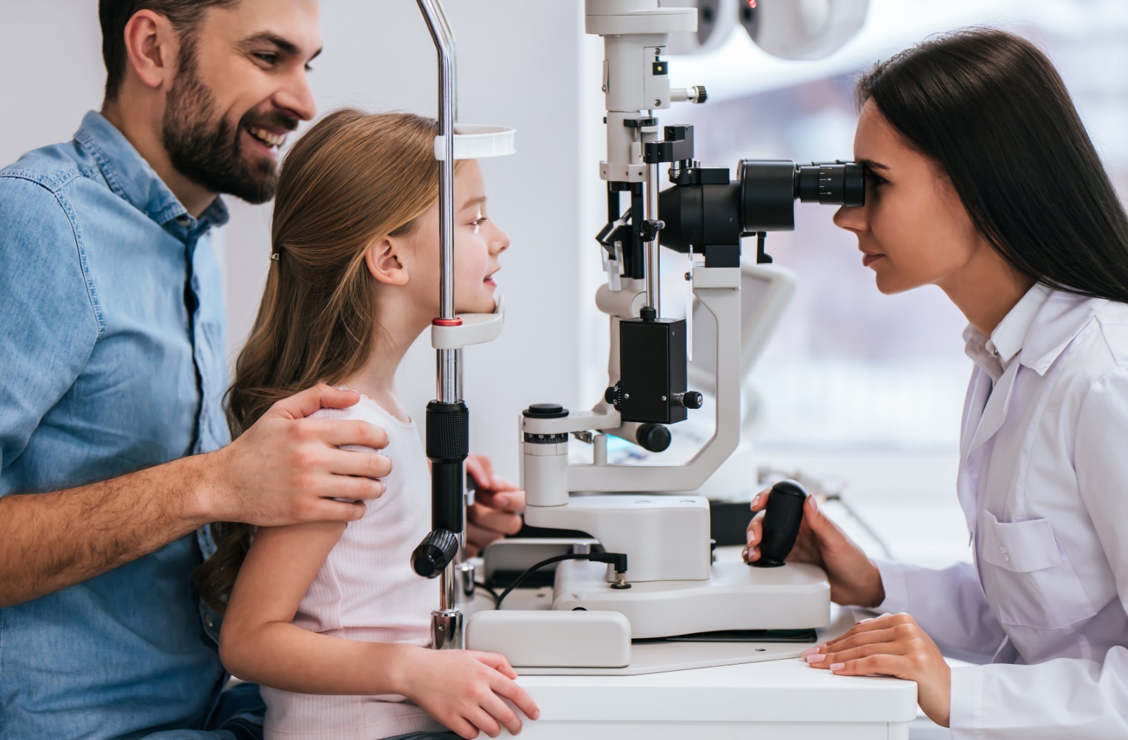 A child sitting on their parent's lap as their optometrist performs a slit lamp exam.