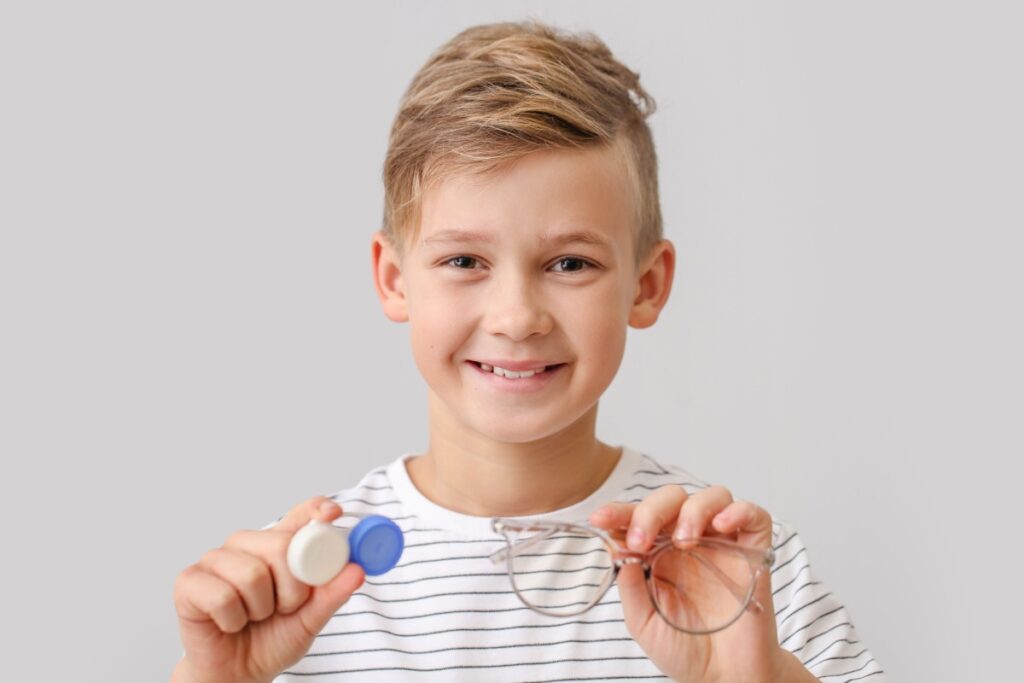 Young smiling boy holding glasses and a contact lenses case.